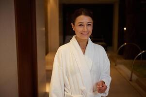 Portrait of a relaxed smiling beautiful elegant middle aged 30- 40 years old European woman in white terry robe enjoying vacation relaxing at spa resort. Recreation, body care and leisure concept photo