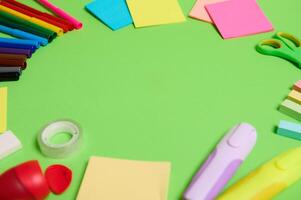 Multi colored assortment of stationery office supplies and school accessories arranged in a circle on light green background, copy space photo