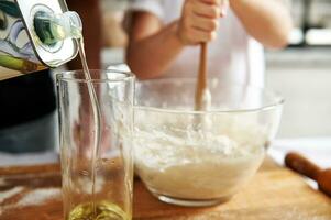 Close-up of pouring olive oil into a glass on a blurred background of a girl kneading dough photo