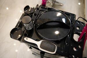 Top view of a hair comb and a set of various hairdressing tools for drying and styling hair on a black cabinet shelf in a barber shop photo