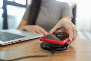 Charging mobile phone battery with wireless charging device in the table. Smartphone charging on a charging pad. Mobile phone near wireless charger Modern lifestyle concept. photo