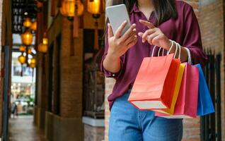 asiático muchachas participación rebaja compras bolsas. consumismo estilo de vida concepto en el compras centro comercial. dama turista caminar compras centrar con compras pantalones foto