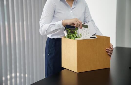 Business woman sending resignation letter and packing Stuff Resign Depress or carrying business cardboard box by desk in office. Change of job or fired from company. photo