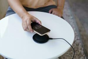 Charging mobile phone battery with wireless charging device in the table. Smartphone charging on a charging pad. Mobile phone near wireless charger Modern lifestyle technology concept. photo