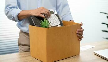 Business man sending resignation letter and packing Stuff Resign Depress or carrying business cardboard box by desk in office. Change of job or fired from company photo