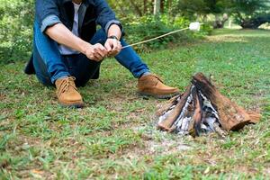 Man warm near campfire in forest and marshmallow on skewers. photo