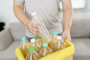 Home recycle eco green zero concept Man throwing empty plastic bottle in recycling bin with yellow garbage bags at home photo