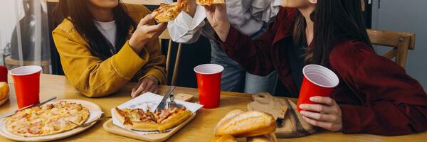 Laughing group of diverse young woman hanging out at home together and eating pizza photo