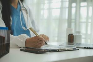 Confident doctor man holding a pill bottle and writing while talking with senior patient and reviewing his medication at office room. photo