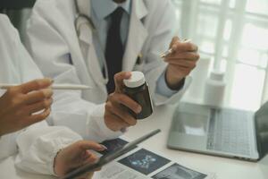 Confident doctor man holding a pill bottle and writing while talking with senior patient and reviewing his medication at office room. photo