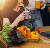 Happy two young women looking laptop computer during cooking together in kitchen room at home. Two young diverse lesbian women spending time together. LGBT and gender identity concept photo