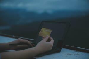 en línea pago, joven mujer participación crédito tarjeta y mecanografía en ordenador portátil foto