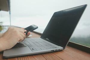 Young man freelancer traveler wearing hat anywhere working online using laptop and enjoying mountains view photo