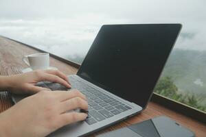 Young man freelancer traveler wearing hat anywhere working online using laptop and enjoying mountains view photo