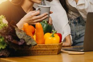 Happy two young women looking laptop computer during cooking together in kitchen room at home. Two young diverse lesbian women spending time together. LGBT and gender identity concept photo