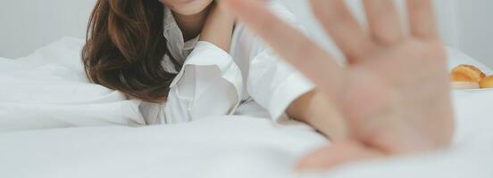 Happy young female in casual clothes smiling and looking at camera while using laptop on bed in bedroom at home photo