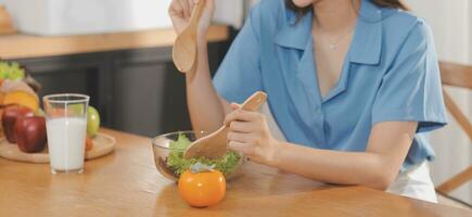 A young woman with a beautiful face in a blue shirt with long hair eating fruit sitting inside the kitchen at home with a laptop and notebook for relaxation, Concept Vacation. photo