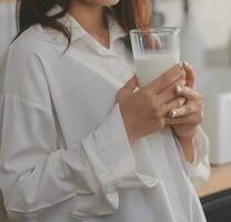 Portrait of a satisfied young asian woman drinking milk from the glass isolated over white background photo