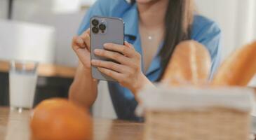 A young woman with a beautiful face in a blue shirt with long hair eating fruit sitting inside the kitchen at home with a laptop and notebook for relaxation, Concept Vacation. photo