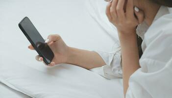 Happy young female in casual clothes smiling and looking at camera while using laptop on bed in bedroom at home photo