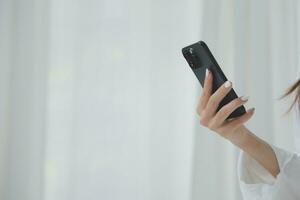 Happy young female in casual clothes smiling and looking at camera while using laptop on bed in bedroom at home photo