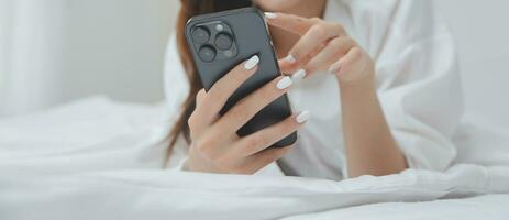 Happy young female in casual clothes smiling and looking at camera while using laptop on bed in bedroom at home photo