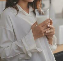 retrato de un satisfecho joven asiático mujer Bebiendo Leche desde el vaso aislado terminado blanco antecedentes foto