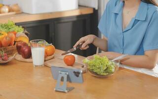 A young woman with a beautiful face in a blue shirt with long hair eating fruit sitting inside the kitchen at home with a laptop and notebook for relaxation, Concept Vacation. photo