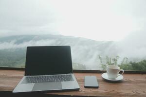 Young man freelancer traveler wearing hat anywhere working online using laptop and enjoying mountains view photo