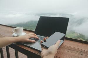 Young man freelancer traveler wearing hat anywhere working online using laptop and enjoying mountains view photo