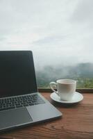 Computer Monitor, Keyboard, coffee cup and Mouse with Blank is on the work table at the sky mountain river and trees front view background. photo