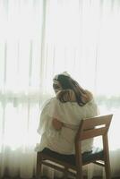 silhouette of woman sitting on the bed beside the windows with sunlight in the morning photo