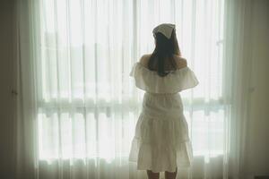 silhouette of woman sitting on the bed beside the windows with sunlight in the morning photo