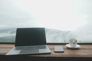 Young man freelancer traveler wearing hat anywhere working online using laptop and enjoying mountains view photo