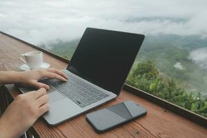 Young man freelancer traveler wearing hat anywhere working online using laptop and enjoying mountains view photo