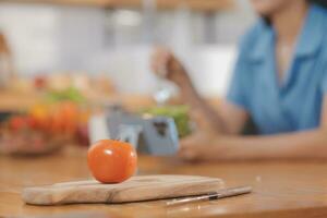 A young woman with a beautiful face in a blue shirt with long hair eating fruit sitting inside the kitchen at home with a laptop and notebook for relaxation, Concept Vacation. photo