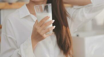 retrato de un satisfecho joven asiático mujer Bebiendo Leche desde el vaso aislado terminado blanco antecedentes foto