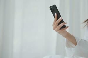 Happy young female in casual clothes smiling and looking at camera while using laptop on bed in bedroom at home photo