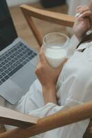 Happy young female in casual clothes smiling and looking at camera while using laptop on bed in bedroom at home photo