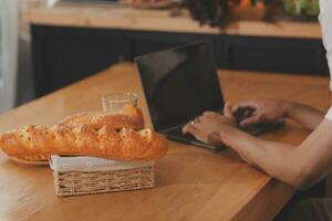 hermoso hombre sentado cerca su esposa a cocina. familia Pareja ver social medios de comunicación, navegar el web mientras sentado a cocina mesa con genérico ordenador portátil. Pareja trabajando con ordenador portátil a hogar foto