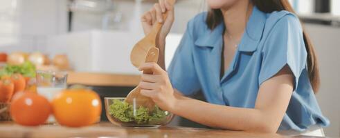 A young woman with a beautiful face in a blue shirt with long hair eating fruit sitting inside the kitchen at home with a laptop and notebook for relaxation, Concept Vacation. photo