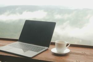 Young man freelancer traveler wearing hat anywhere working online using laptop and enjoying mountains view photo