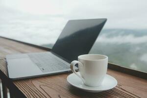 Young man freelancer traveler wearing hat anywhere working online using laptop and enjoying mountains view photo