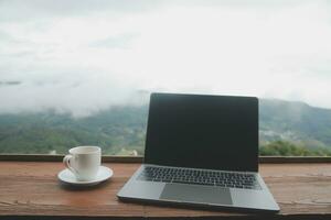 Computer Monitor, Keyboard, coffee cup and Mouse with Blank is on the work table at the sky mountain river and trees front view background. photo