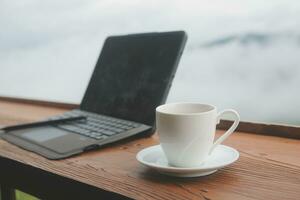 Computer Monitor, Keyboard, coffee cup and Mouse with Blank is on the work table at the sky mountain river and trees front view background. photo