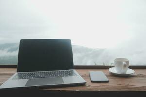 Young man freelancer traveler wearing hat anywhere working online using laptop and enjoying mountains view photo