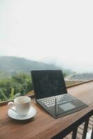 Computer Monitor, Keyboard, coffee cup and Mouse with Blank is on the work table at the sky mountain river and trees front view background. photo