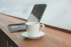 Computer Monitor, Keyboard, coffee cup and Mouse with Blank is on the work table at the sky mountain river and trees front view background. photo