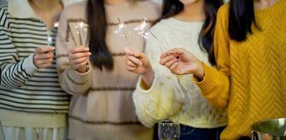 Cheerful friends enjoying home Birthday holiday party. Asian Friends hold lights with sparkling Sparkler celebrating Christmas or New Year eve party. photo