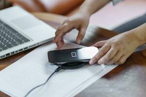 Charging mobile phone battery with wireless charging device in the table. Smartphone charging on a charging pad. Mobile phone near wireless charger Modern lifestyle technology concept photo